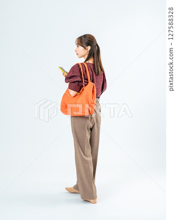 Full-body photo of a woman in casual wear walking with a smartphone Full-body photo of a woman in casual wear walking with a smartphone 127588328