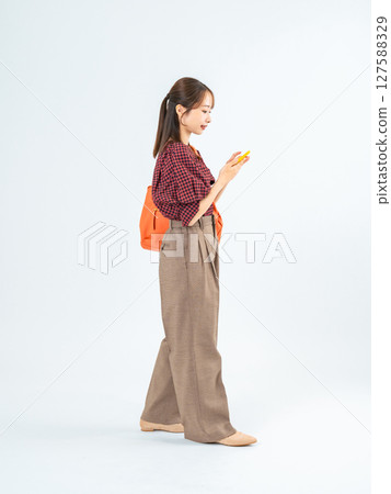 Full-body photo of a woman in casual wear walking with a smartphone Full-body photo of a woman in casual wear walking with a smartphone 127588329