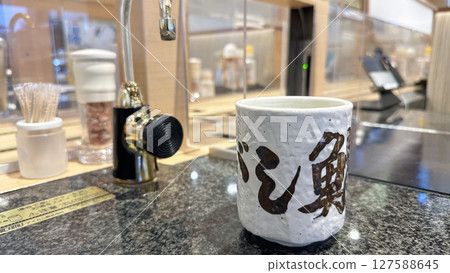 Hot water dispenser and teacups installed at a conveyor-belt sushi restaurant 127588645