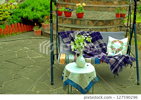 Apple blossoms on a table in front of a sofa swing in the courtyard of a country house. 127590296
