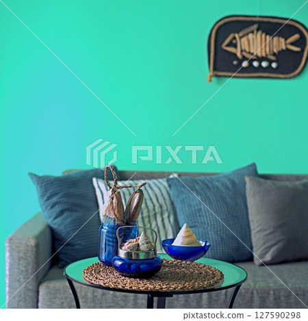 Marine style in the apartment interior - a sofa with pillows and a table with shells and fish figures. Marine style in the apartment interior - a sofa with pillows and a table with shells and fish figures. 127590298