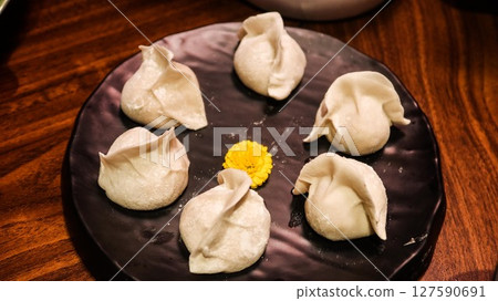 close up of six uncooked raw pork dumplings (Jiaozi or Gyoza) on a plate with a yellow flower in the middle for decoration 127590691
