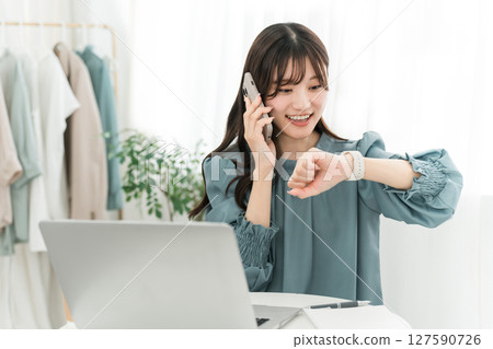 A stylish young Asian woman using a computer while talking on her smartphone A stylish young Asian woman using a computer while talking on her smartphone 127590726
