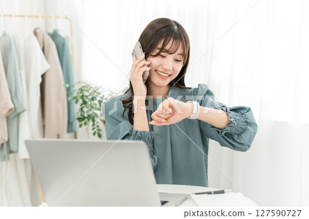 A stylish young Asian woman using a computer while talking on her smartphone A stylish young Asian woman using a computer while talking on her smartphone 127590727