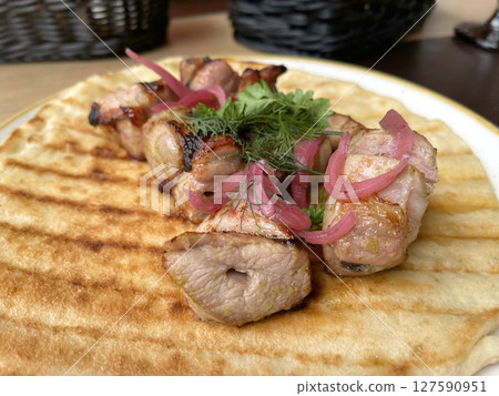 Chunks of grilled meat with pickled onions on pancake, pita. Asian traditional cuisine. Food and products. 127590951