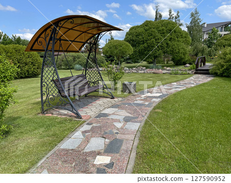 Foot path of colorful tile pieces and swings in park. Green lawn and trees in summer on sunny day. Background for design. Ecology and nature. Landscape design. Foot path of colorful tile pieces and swings in park. Green lawn and trees in summer on sunny day. Background for design. Ecology and nature. Landscape design. 127590952
