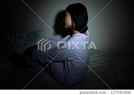 Worried young woman sitting on bed in the dark 127591006
