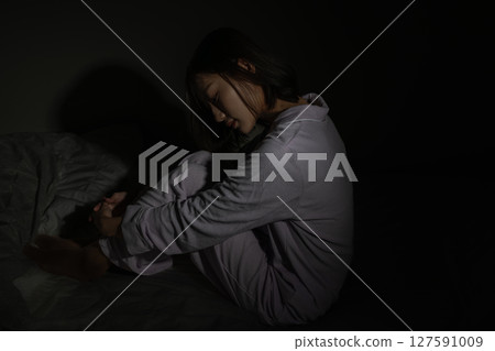 Worried young woman sitting on bed in the dark 127591009