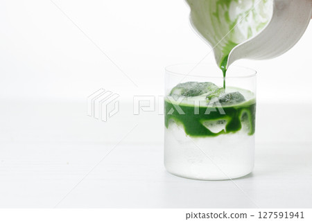 fresh matcha tea, green tea pouring on a glass of coconut water on white wooden table. 127591941