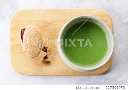 Cup of fresh matcha tea, green tea and Taiyaki, Japanese fish-shaped cake, filled with Anko or red bean on wooden plate. Cup of fresh matcha tea, green tea and Taiyaki, Japanese fish-shaped cake, filled with Anko or red bean on wooden plate. 127591953
