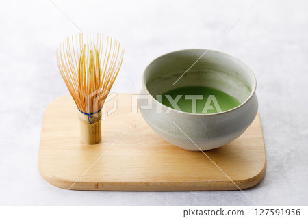 Cup of fresh matcha tea, green tea and Chasen, bamboo whisk, on wooden plate on white table. 127591956