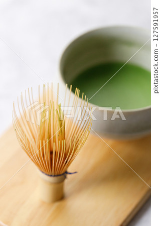 Cup of fresh matcha tea, green tea and Chasen, bamboo whisk, on wooden plate on white table. 127591957
