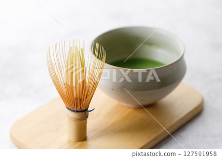Cup of fresh matcha tea, green tea and Chasen, bamboo whisk, on wooden plate on white table. 127591958