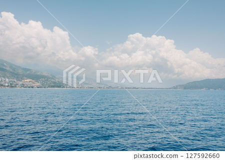 Scenic coastal landscape with blue sea, mountain ridge and dramatic clouds over a Mediterranean town. Summer travel, nature and seascape concept. Clouds descend on the mountains. Scenic coastal landscape with blue sea, mountain ridge and dramatic clouds over a Mediterranean town. Summer travel, nature and seascape concept. Clouds descend on the mountains. 127592660