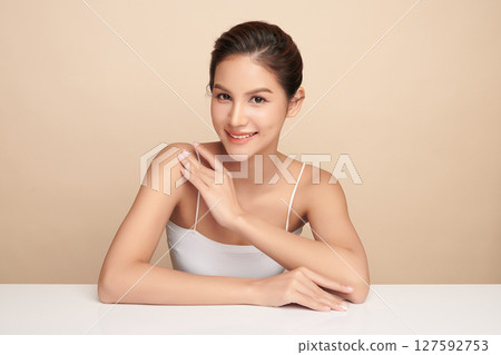 A beautiful young Asian woman with clean, fresh skin against a beige background. Skincare, facial treatment, cosmetology, beauty, and spa. An elegant portrait of an Asian woman. 127592753