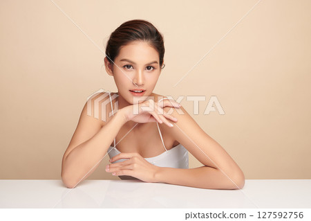 A beautiful young Asian woman with clean, fresh skin against a beige background. Skincare, facial treatment, cosmetology, beauty, and spa. An elegant portrait of an Asian woman. 127592756