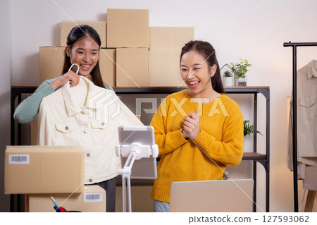 Two young asian woman live online clothing store while showing clothing with tablet and laptop. Two young asian woman live online clothing store while showing clothing with tablet and laptop. 127593062
