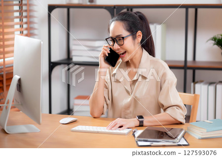 Young asian business woman using desktop computer while talking with smart phone in home office. 127593076