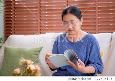 Asian senior woman reading a book sitting on sofa with relax in living room at home. Asian senior woman reading a book sitting on sofa with relax in living room at home. 127593103