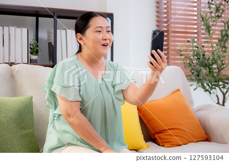 Asian senior woman smiling video call with smartphone in cozy living room at home. Asian senior woman smiling video call with smartphone in cozy living room at home. 127593104
