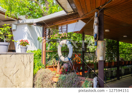 Outdoor garden cafe with life preserver and potted plants. Relaxing summer atmosphere, greenery, and nautical themed decor. Outdoor garden cafe with life preserver and potted plants. Relaxing summer atmosphere, greenery, and nautical themed decor. 127594151