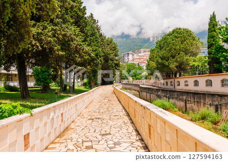 Scenic walkway in Budva with stone pavement and cypress trees. Urban nature, peaceful atmosphere and summer strolls in Montenegro. 127594163