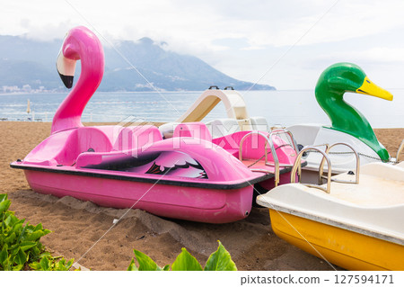 Colorful flamingo and duck paddle boats on the beach before summer rides. Playful seaside leisure, family vacation and coastal amusement atmosphere. Colorful flamingo and duck paddle boats on the beach before summer rides. Playful seaside leisure, family vacation and coastal amusement atmosphere. 127594171