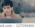 一名 20 多歲的男子在戶外看著電腦 127594460