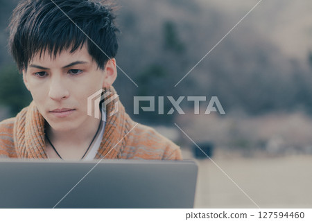 A man in his 20s looking at a computer outdoors 127594460