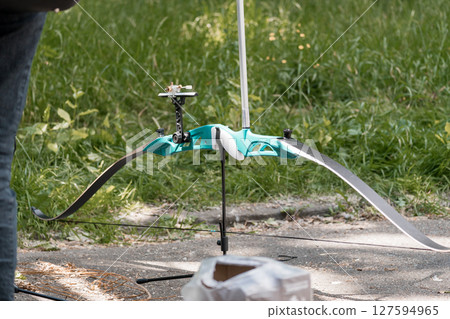 Teal Recurve Bow with Stabilizer Standing Outdoors on Grass and Pavement, Archery Equipment, Sport Practice, Bright Summer Day Teal Recurve Bow with Stabilizer Standing Outdoors on Grass and Pavement, Archery Equipment, Sport Practice, Bright Summer Day 127594965