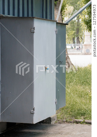 Gray Metal Electrical Box with Blue Lock Outdoor, Park Power Cabinet Scene, Utility Infrastructure, Security, Industrial Texture, Dim Daylight. Gray Metal Electrical Box with Blue Lock Outdoor, Park Power Cabinet Scene, Utility Infrastructure, Security, Industrial Texture, Dim Daylight. 127594973