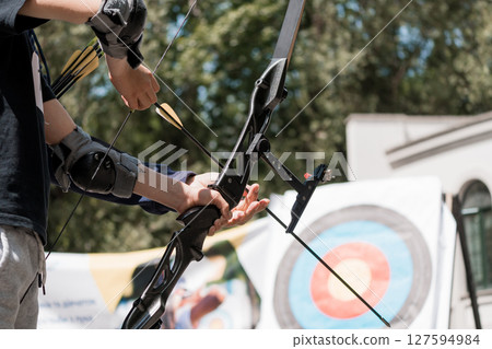 Archery Practice in Sunlight: Close-Up of Archer Drawing Bow with Arrows Aimed at Target Outdoors, Blue Shirt, Focused Action 127594984