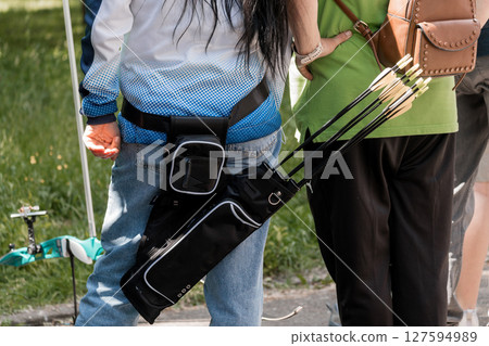 Archery Practice Outdoors: Close-Up of Archer's Equipment Belt, Arrows, Green Field, Summer Sunlight, Casual Clothing, Black and Blue Textures. Archery Practice Outdoors: Close-Up of Archer's Equipment Belt, Arrows, Green Field, Summer Sunlight, Casual Clothing, Black and Blue Textures. 127594989