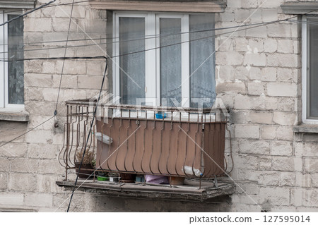 Urban Balcony Still Life with Pigeons: Rusty Metal Railing, Net Curtains, and Concrete Facade in Pale Grey Tones 127595014