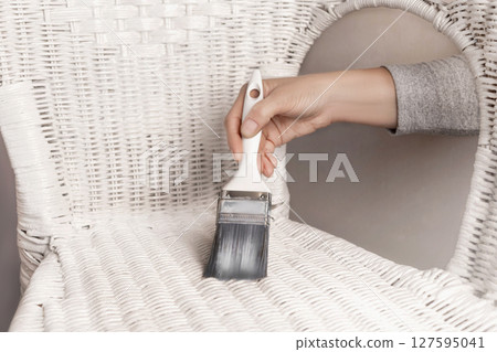 A woman paints an old white rattan chair with a brush. Updates DIY photo 127595041
