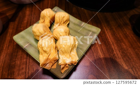 Show title suggestion close up of six pieces of uncooked raw shrimp and pork stuffed dumplings on a plate on a wooden table with copy space 127595672
