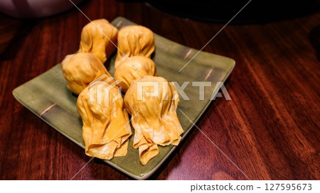 close up of six pieces of uncooked raw shrimp and pork stuffed dumplings on a plate on a wooden table with copy space 127595673