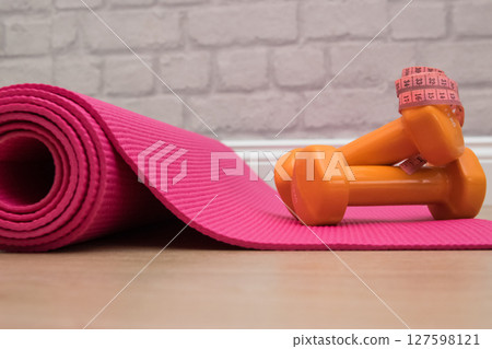 Two orange dumbbells on a pink yoga mat in fitness studie. A tools for training, sport and activity in summer time. Two orange dumbbells on a pink yoga mat in fitness studie. A tools for training, sport and activity in summer time. 127598121