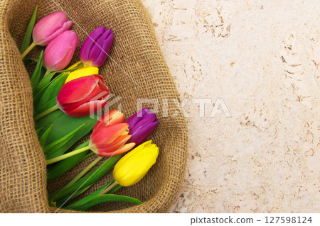 Multicolor tulips bouquet in natural fabric wrapping paper. Spring flowers on the cork background . Top view with place for text. Copy space. Multicolor tulips bouquet in natural fabric wrapping paper. Spring flowers on the cork background . Top view with place for text. Copy space. 127598124