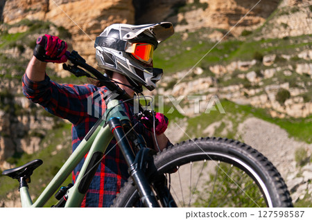 Male athlete cyclist in helmet and protective mask outdoors. MTB rider in mountainous terrain against the backdrop of epic rocks. 127598587
