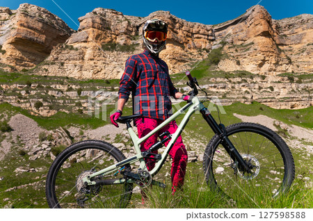 Male athlete cyclist in helmet and protective mask outdoors. MTB rider in mountainous terrain against the backdrop of epic rocks. 127598588
