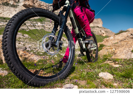 Close up of extreme mountain biking, cyclist riding off-piste in green field with mountains in background, outdoor fun and enjoying riding Close up of extreme mountain biking, cyclist riding off-piste in green field with mountains in background, outdoor fun and enjoying riding 127598606