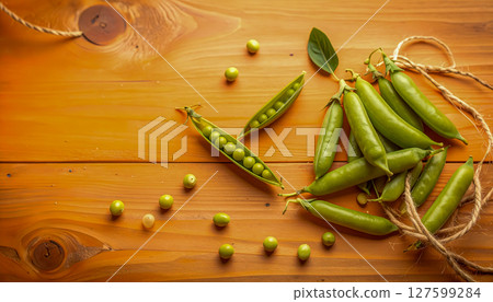 A bunch of green peas are on a wooden table. The peas are scattered around the table and some are in a pile 127599284