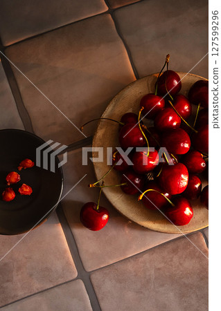 Fresh Juicy Red Cherries on Beige Ceramic Plate Next to Bowl with Cherry Pits on a Tile Surface. Fresh Juicy Red Cherries on Beige Ceramic Plate Next to Bowl with Cherry Pits on a Tile Surface. 127599296