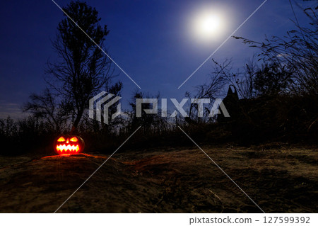 Spooky Halloween pumpkin jack-o-lantern with burning candles in scary forest at night Spooky Halloween pumpkin jack-o-lantern with burning candles in scary forest at night 127599392