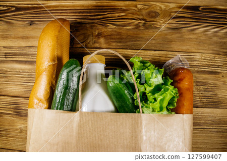 Paper bag with different food on wooden table. Top view. Grocery shopping concept Paper bag with different food on wooden table. Top view. Grocery shopping concept 127599407