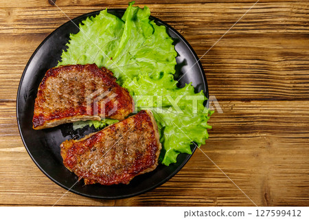 Grilled pork steaks with lettuce leaves on wooden table. Top view 127599412