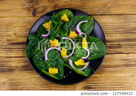 Tasty salad with spinach, orange, red onion and sesame seeds on wooden table. Top view. Healthy food or vegetarian concept 127599432