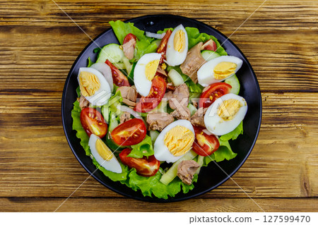 Tasty tuna salad with eggs, lettuce and fresh vegetables on wooden table. Top view 127599470