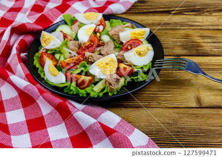 Tasty tuna salad with eggs, lettuce and fresh vegetables on wooden table 127599471